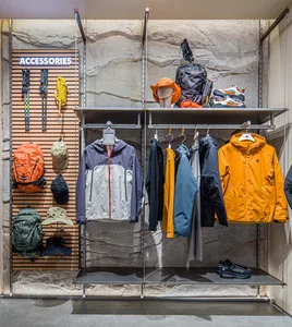 A retail store display featuring jackets and accessories arranged on metal shelves against a stone background.