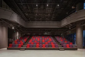 Empty industrial-style auditorium with metal seats, black ceiling structure, and concrete floor.
