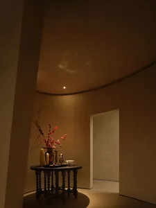 A minimalist living room with a wooden platform and a table with candles and a vase containing branches and flowers on a circ