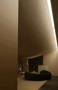 A modern living room with concrete walls, a circular sofa, and a fireplace with a small fire burning.