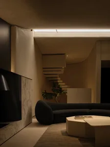 A modern living room with exposed concrete walls, a spiral staircase, and a curved sofa.