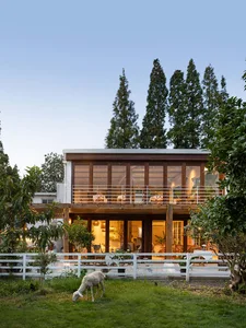 A two-story modern rural family home with large windows and a wooden exterior.