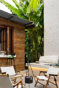 Minimalist outdoor living space featuring a wooden structure and white seating area surrounded by greenery and palm trees.