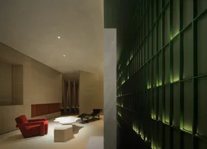 A modern hotel lobby featuring concrete walls, a red armchair, and green accent lighting.