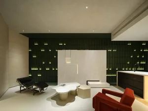 Modern minimalist living space featuring a lounge chair, red armchair, and abstract marble table with green illuminated backg