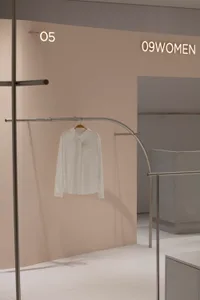 極簡服裝店內，白衣掛在金屬衣架上，地面為混凝土。