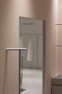 A minimalist clothing boutique featuring white walls, a glass wall, and a white dress hanging on a rail.