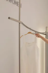 A person holding a white dress on a wooden hanger, displayed on a clothing rack