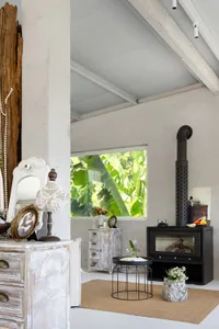 A spacious industrial living room with concrete walls and ceiling, large open windows, and a black stove with a natural wood 