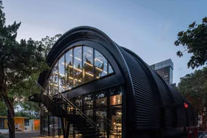 A modern, black metal-clad building exterior with large glass windows and a curved roof.