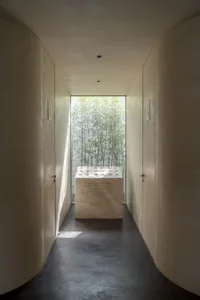 A modern, minimalist corridor featuring a concrete floor and walls with a large window showcasing green bamboo plants.
