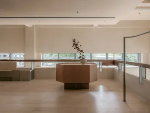 A minimalist lobby with brown wooden furniture, white walls, and large windows.