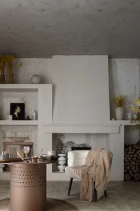 A modern minimalist living room with a concrete fireplace, wooden armchair with a beige throw blanket, and a circular metalli