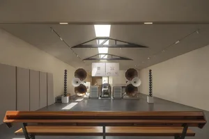 A spacious modern music studio with concrete flooring and walls, equipped with large speakers and musical equipment.