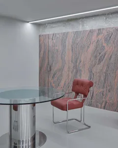 A modern office space with a sleek, curved glass table, a red leather chair with metal frame, and a concrete wall with marble
