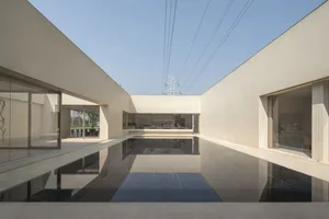 Modern residential interior with concrete walls and floor, featuring large windows and a central reflective pool.