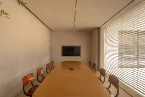 A modern, industrial-style meeting room with a long wooden table, wooden chairs, concrete walls, and concrete floor, featurin