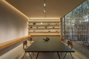 A modern conference room featuring a table, chairs, and shelves with bags, surrounded by a bamboo garden.
