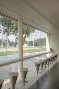 Modern minimalist cafe with concrete and glass materials, featuring cone-shaped stools along a glass-enclosed window.