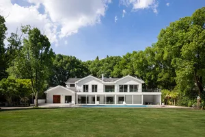 A modern residential house with white painted exterior and glass walls surrounded by greenery.