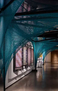 Modern architecture exhibition space with turquoise metal cable net ceiling structure.
