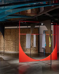 Modern retail space featuring a red metal frame display with textiles hanging on it.