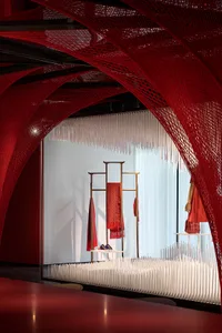 Fashion retail shop with red netting covering the ceiling and walls, featuring clothing racks and display stands.