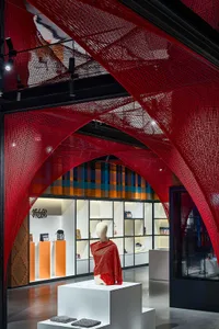 A retail store display featuring a mannequin draped in a red-netted garment, surrounded by a red-netted structure and various