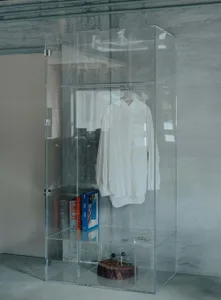 A minimalist glass display closet featuring a white shirt on a hanger.