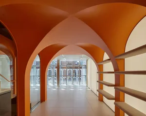 A modern lobby featuring orange concrete arches and shelving units with cushioned benches.