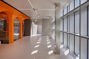 A modern office hallway with concrete walls and flooring, featuring arched doorways and windows.