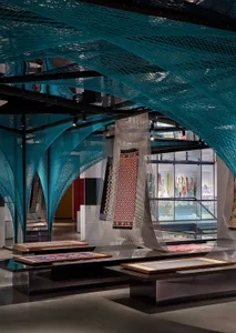 A modern retail store display featuring intricate blue netting and colorful textiles on tables and shelves.