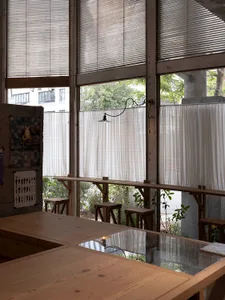 A cozy coffee shop interior features natural wood tables, white curtains, and industrial-style lighting.