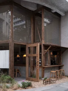 Wood and concrete exterior of a restaurant with large windows and open seating area.