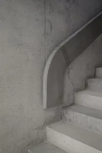 A modern, minimalist concrete staircase with smooth, curved risers against a textured concrete wall.