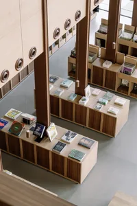 A modern library with wooden floors and furniture, showcasing a well-organized space with books displayed on tables and shelv