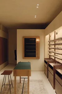 A modern retail store interior featuring wooden shelves and a green countertop with a stool.