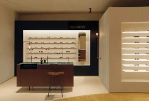 一間現代太陽眼鏡店，展示櫃內有多層擺放太陽眼鏡的層架，旁邊有木質凳子與櫃檯。