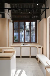 Interior of a minimalist coffee shop featuring wooden furniture and materials, with a large window providing natural light.