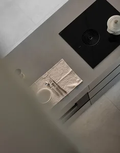 A minimalist kitchen counter featuring a concrete countertop with a plate, cutlery, and a pot, viewed from above.