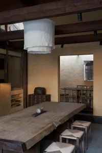 A minimalist residential dining space featuring wooden furniture and a white hanging lamp.