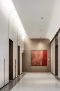 簡潔的極簡走廊，混凝土牆面搭配紅色抽象壁畫，弧形天花板燈光照亮電梯入口