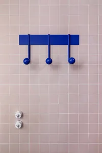 Modern minimalist interior design featuring a set of blue metal hooks mounted on a pink tiled wall.