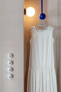 A white dress hanging on a hanger mounted on a wall with pink ceramic tiles.