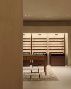 Modern minimalist optical store featuring wooden shelves and display furniture with an array of eyeglasses.