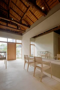 A minimalistic cafe space with wooden furnishings and concrete walls, illuminated by warm lighting.
