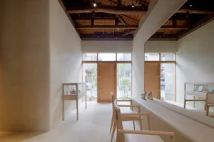 A minimalist storefront featuring wooden elements and concrete surfaces with a large glass window and a wooden door.