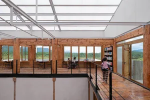 A modern library interior featuring exposed wooden beams and extensive glass walls, with people engaged in reading and studyi