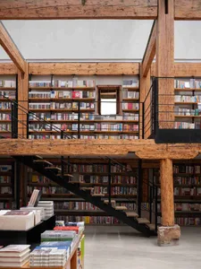 A modern library with wooden shelves and a metal staircase, showcasing a collection of books.