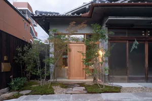 An exterior view of a traditional Japanese residence featuring wooden doors, concrete walls, and glass elements.
